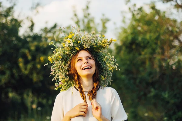 Menina bonita na grinalda de flores no prado no dia ensolarado. Retrato de jovem mulher bonita vestindo uma coroa de flores silvestres. Jovem pagão eslavo menina cerimônia de conduta no verão . Imagem De Stock