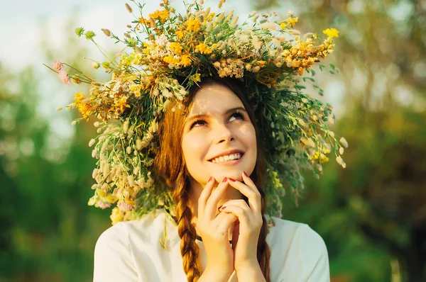 Menina bonita na grinalda de flores no prado no dia ensolarado. Retrato de jovem mulher bonita vestindo uma coroa de flores silvestres. Jovem pagão eslavo menina cerimônia de conduta no verão . Imagens Royalty-Free
