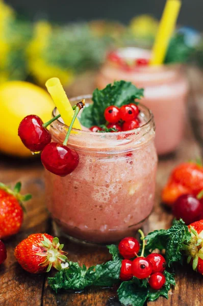 muz ve çilek güler yüzlü. Mutfak masasında malzemelerle bardaklarda iki soğuk çilek muz Smoothies. Çilek Muz Smoothie taze malzemelerle hazırlanan. Taze çilek güler yüzlü