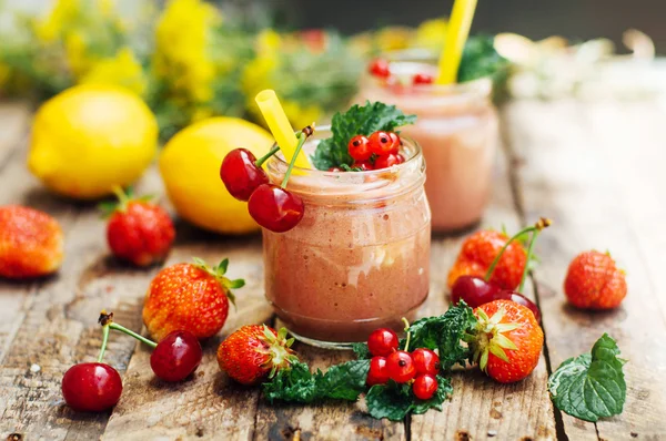 muz ve çilek güler yüzlü. Mutfak masasında malzemelerle bardaklarda iki soğuk çilek muz Smoothies. Çilek Muz Smoothie taze malzemelerle hazırlanan. Taze çilek güler yüzlü