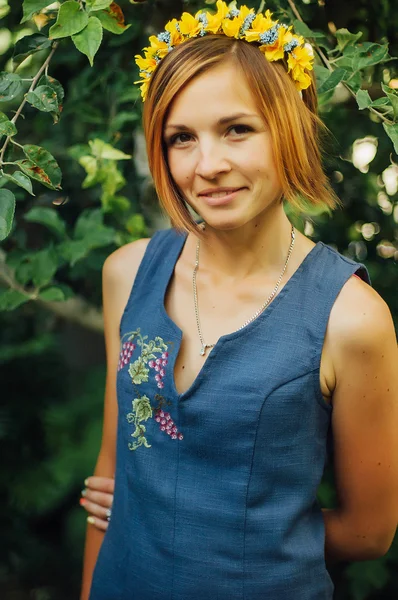 Portrait of a beautiful young woman wearing wreath. Young beautiful woman posing with flowers bouquet on her head. Girl posing in a decorative wreath of artificial flowers on outdoor in the summer