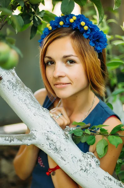 Ritratto di una bellissima giovane donna che indossa la corona. Giovane bella donna in posa con mazzo di fiori sulla testa. Ragazza in posa in una corona decorativa di fiori artificiali all'aperto in estate — Foto Stock