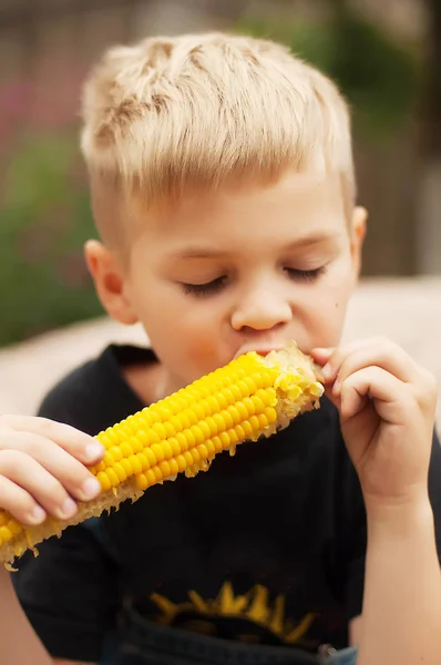 Jongen met maïs op de kolf in de achtertuin. Een jongen gelukkig ab — Stockfoto