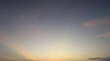 A serene dawn sky at sunrise with soft crepuscular rays subtly piercing through wispy clouds, displaying a beautiful color gradient from cool blues to warm pinks and yellows.