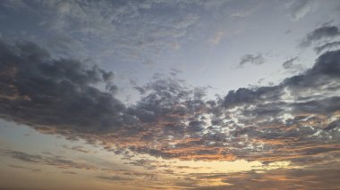 Koyu kümülüs ve benekli altokümülüs bulutlarından oluşan çarpıcı, çarpıcı bir gündoğumu gökyüzü aşağıdan parlak bir şekilde aydınlatılıyor. Sıcak turuncu ve sarı ışık serin mavi-gri gökyüzü ile çelişiyor.