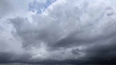 Yoğun bir bulut ağır, koyu gri fırtına bulutları tarafından hükmedilmiş, küçük bir mavi gökyüzü parçası sol üstte görünür, uğursuz bir havanın yaklaştığını hisseder..