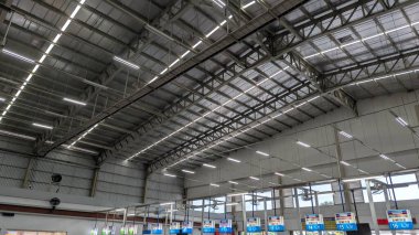 Karanganyar, Endonezya, Mart 02, 2026, alçak açılı bir çekim geniş bir sanayi deposunun içindeki devasa endüstriyel tavanı yakalar. Uzun sıralı parlak aydınlatma armatürleri kıvrımlı çatı panellerini, çelik kirişleri aydınlatıyor. Geniş perspektif