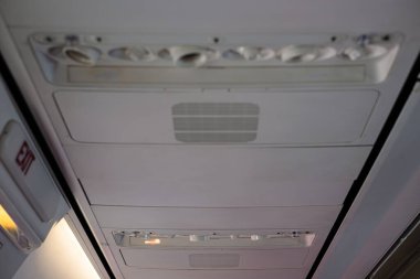 Uçuş sırasında uçak kabin tavanı çıkış işaretini, havalandırma sistemini ve yolcu kontrol panellerini gösteriyor. Güvenlik teknolojisini vurguluyor..