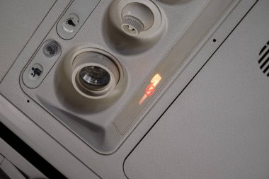 Bir uçak kabin panelinin yakın çekimi sigara içilmediğini, ışık düğmesi okunmadığını ve havalandırma kontrollerinin uçuş sırasında modern iç teknolojiyi vurguladığını gösteriyor..