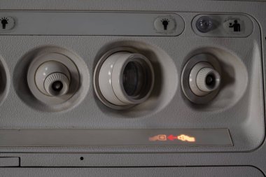 Üzerimizde ayarlanabilir hava delikleri, kontrol düğmeleri ve ticari bir uçak kabininin içinde emniyet tasarımı ve teknolojisini ön plana çıkaran kemer işaretini gösteren uçak konsolu var..