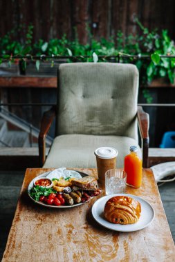 Sıcak bir kafede, ahşap bir masada servis edilen kruvasan ve kahveyle yapılan tam İngiliz kahvaltısı, otantik yerel yemek ve seyahat ve yemek temaları için konukseverlik tasvir ediliyor..