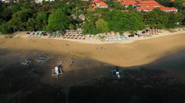 Sanur sahil şeridi boyunca geriye doğru hareket eden hava aracı görüntüsü ve Endonezya, Bali 'de tatil beldeleri; Hint Okyanusu ve beyaz kum kıyılarını gösteren tropikal bir doğa plakası.