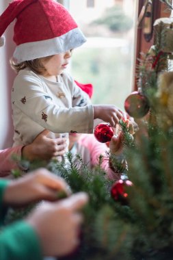 Noel Baba şapkalı küçük çocuk evde Noel ağacı süslüyordu büyük kardeşinin yardımıyla.