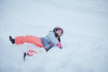 Yüksek açılı kar manzaralı, kasklı ve kayak elbiseli gülümseyen küçük kız.