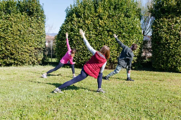 Güneşli bir günde parkta egzersiz yapan üç yetişkinin arka görüntüsü
