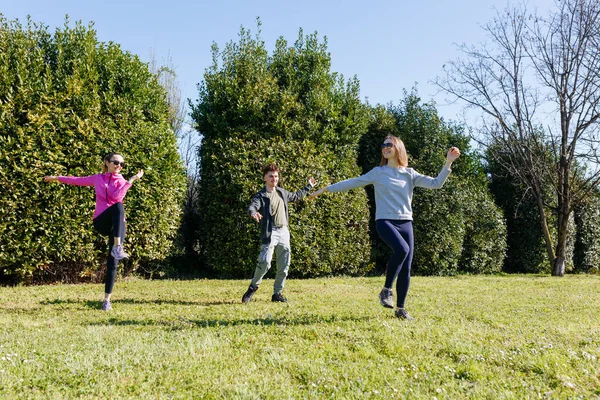 Parkta egzersiz yapan üç gülümseyen kişinin tam boy görünümü