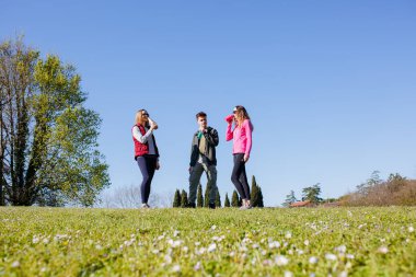 Tepenin tepesinde birlikte duran üç kişi şişelerden su içiyor ve konuşuyor.