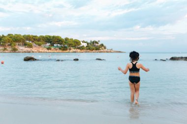Güneşli bir günde, mayo giymiş bir kızın sahile girişinin arka görüntüsü.