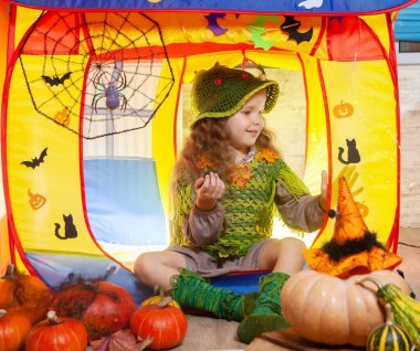 Orman perisi gibi giyinmiş küçük tatlı bir kız Cadılar Bayramı için süslenmiş bir çocuk çadırında oturuyor. Yarasalar ve hayaletler, örümcekli örümcek ağı, turuncu balkabağı..