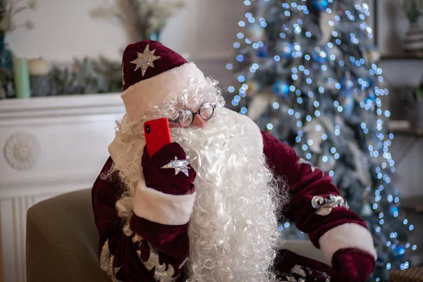 모자를 곱슬곱슬 수염을 산타클로스는 스마트폰에서 크리스마스 인사를 — 스톡 사진