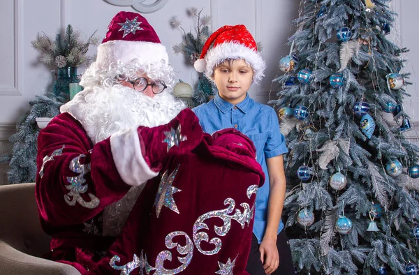 Noel Baba Kırmızı Şapkalı Bir Çocuk Noel Ağacının Yanında Oturuyorlar — Stok fotoğraf