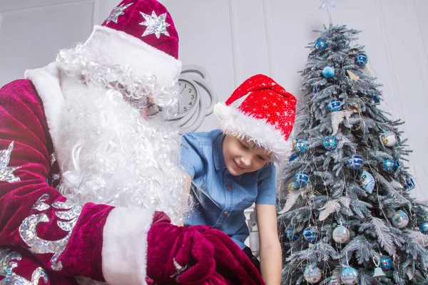 산타클로스와 모자를 소년이 크리스마스 있습니다 아이는 산타의 가방을 들여다보고 선물을 — 스톡 사진