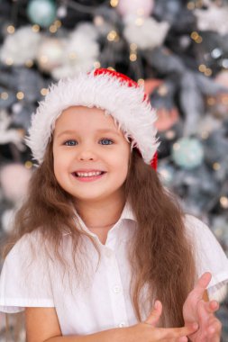 Yeni yıl portresi, Noel Baba şapkalı şirin bir çocuk, yeni yıl ağacının arka planında, Noel havası, kış tatili, bebek kahkahaları..