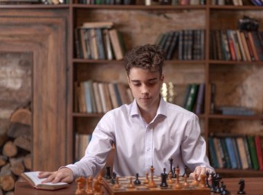 Genç kendi kendine satranç oynar, büyük tahta bir masada oturur ve satranç hamlelerini düşünür, beyaz ve siyah satranç taşları, satranç ve şah mat..