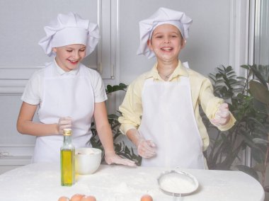 Aşçı gibi giyinmiş iki tatlı Avrupalı çocuk un, süt ve yumurta yoğuruyor, çocuklar mutfakta oynuyor, gençler hamurdan turta yapıyor..