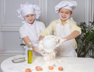 Aşçı gibi giyinmiş iki tatlı Avrupalı çocuk un, süt ve yumurta yoğuruyor, çocuklar mutfakta oynuyor, gençler hamurdan turta yapıyor..