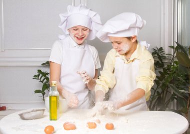 Aşçı gibi giyinmiş iki tatlı Avrupalı çocuk un, süt ve yumurta yoğuruyorlar, çocuklar mutfakta oynuyorlar.