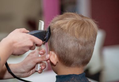 Küçük tatlı bir çocuk kuaförde oturuyor, bir okul çocuğu kuaförde saçını kestiriyor, bir çocuk berber dükkanında, kısa erkek tıraşı oluyor..