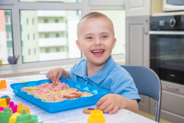 Down sendromlu şirin bir çocuğun portresi, modellik için kum ve kalıplarla oynayan bir çocuk, erken gelişim, çocuklar ve valeler..