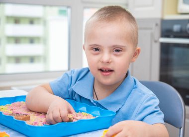 Down sendromlu şirin bir çocuğun portresi, modellik için kum ve kalıplarla oynayan bir çocuk, erken gelişim, çocuklar ve valeler..