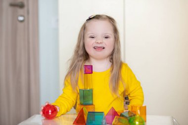 Down sendromlu güzel bir kız inşaatçı, parlak saydam figürler, engelli bir çocuğun erken gelişimi ile oynuyor..