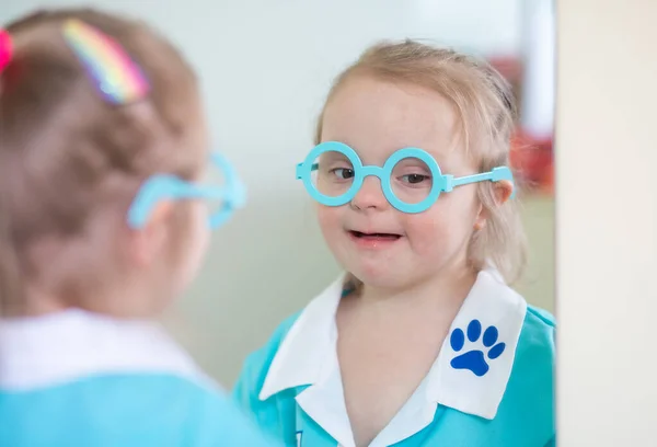Down syndrome in a little girl, a child in a doctor\'s costume playing with a doll and with medical instruments, disabled children, genetic mental illness, an extra chromosome in humans.