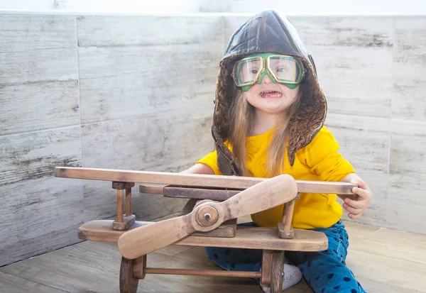 Down syndrome in a little girl, a child sitting near a wooden model of an airplane, a girl in a pilot\'s helmet, disabled child, a genetic mental illness, an extra chromosome in humans.