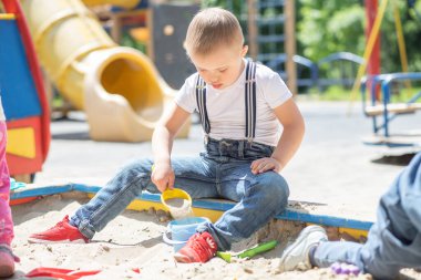 Down sendromlu bir çocuk kum havuzunda oynuyor, bir çocuk kum kazıyor, çocuk eğlencesi, engelli çocuklar için hoşgörü,.