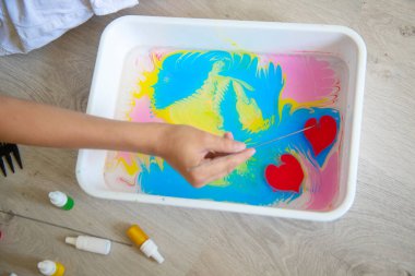 Suyun üzerinde iğneyle çizim yapan çocuk, Ebru tekniği.