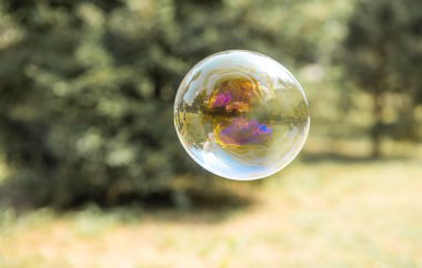 Mutlu bir kız büyük sabun köpükleri yakalar, bir çocuk sokakta oynar, havada hafif balonlar süzülür..