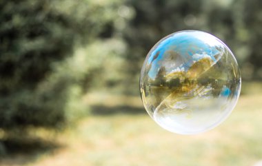 Mutlu bir kız büyük sabun köpükleri yakalar, bir çocuk sokakta oynar, havada hafif balonlar süzülür..