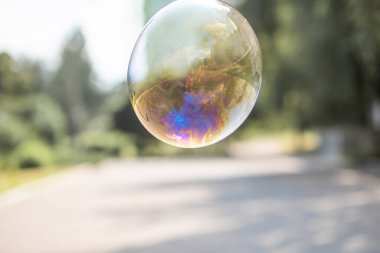 Mutlu bir kız büyük sabun köpükleri yakalar, bir çocuk sokakta oynar, havada hafif balonlar süzülür..