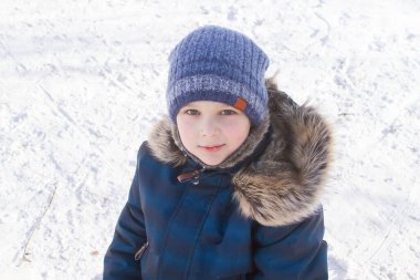 Kışlık giysiler içinde yakışıklı bir çocuğun portresi, anlamlı gözler, parlak yanaklar ve bir okul çocuğunun güzel bir gülümsemesi, bir çocuk kışın karlı dağlarda dinleniyor.