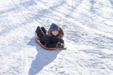 Kışlık giysiler içinde yakışıklı bir çocuğun portresi, anlamlı gözler, parlak yanaklar ve bir okul çocuğunun güzel bir gülümsemesi, bir çocuk kışın karlı dağlarda dinleniyor.
