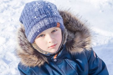 Kışlık giysiler içinde yakışıklı bir çocuğun portresi, anlamlı gözler, parlak yanaklar ve bir okul çocuğunun güzel bir gülümsemesi, bir çocuk kışın karlı dağlarda dinleniyor.