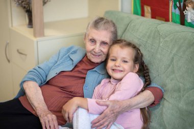 Yaşlı bir kadın ve küçük bir kızın portresi, büyükannesi torununa sarılıyor, aile bağları, yaşlılık ve gençlik, 90 yaşında, yaşlı bir yüzdeki kırışıklıklar, güzel bir yaşlılık, bir kadın ve bir çocuk.