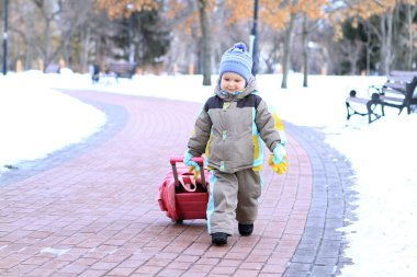Büyüleyici bir parkta, mutlu küçük bir çocuk dolambaçlı bir yolda ilerliyor, arkasında parlak kırmızı bir araba çekiyor. Etrafındaki ağaçlardan süzülen yapraklar gibi kar zemini kaplıyor..