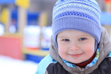 Sıcak kışlık kıyafetli neşeli bir çocuk, karla kaplı canlı bir oyun alanında oynamaktan zevk alır. Parlak gülüşü serin sahnede neşe saçıyor..