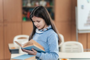 Meraklı bir bakışla, bir liseli kız canlı bir sınıfta duruyor, bir kitaba dalmış. Sınıf arkadaşları tarafından çevrelenmiş yeni hikayeler keşfederken usulca gülümseyerek ders çalışmaktan zevk alıyor..