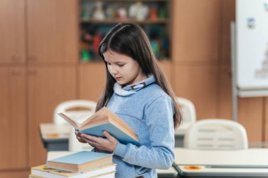 Canlı bir sınıfta, odaklanmış bir liseli kız renkli raflar ve kitaplarla çevrili, merak ve eğitim ruhunu somutlaştıran bir kitap okur..